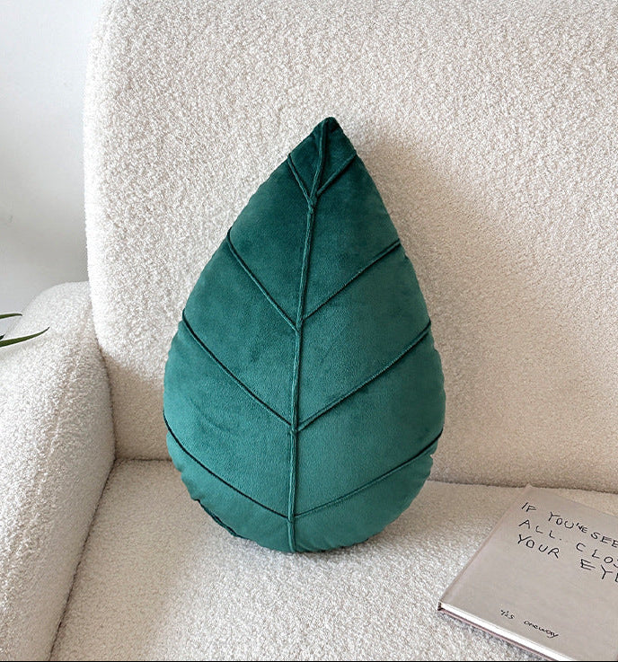 Teal leaf-shaped pillow on a beige sofa with a white wall background