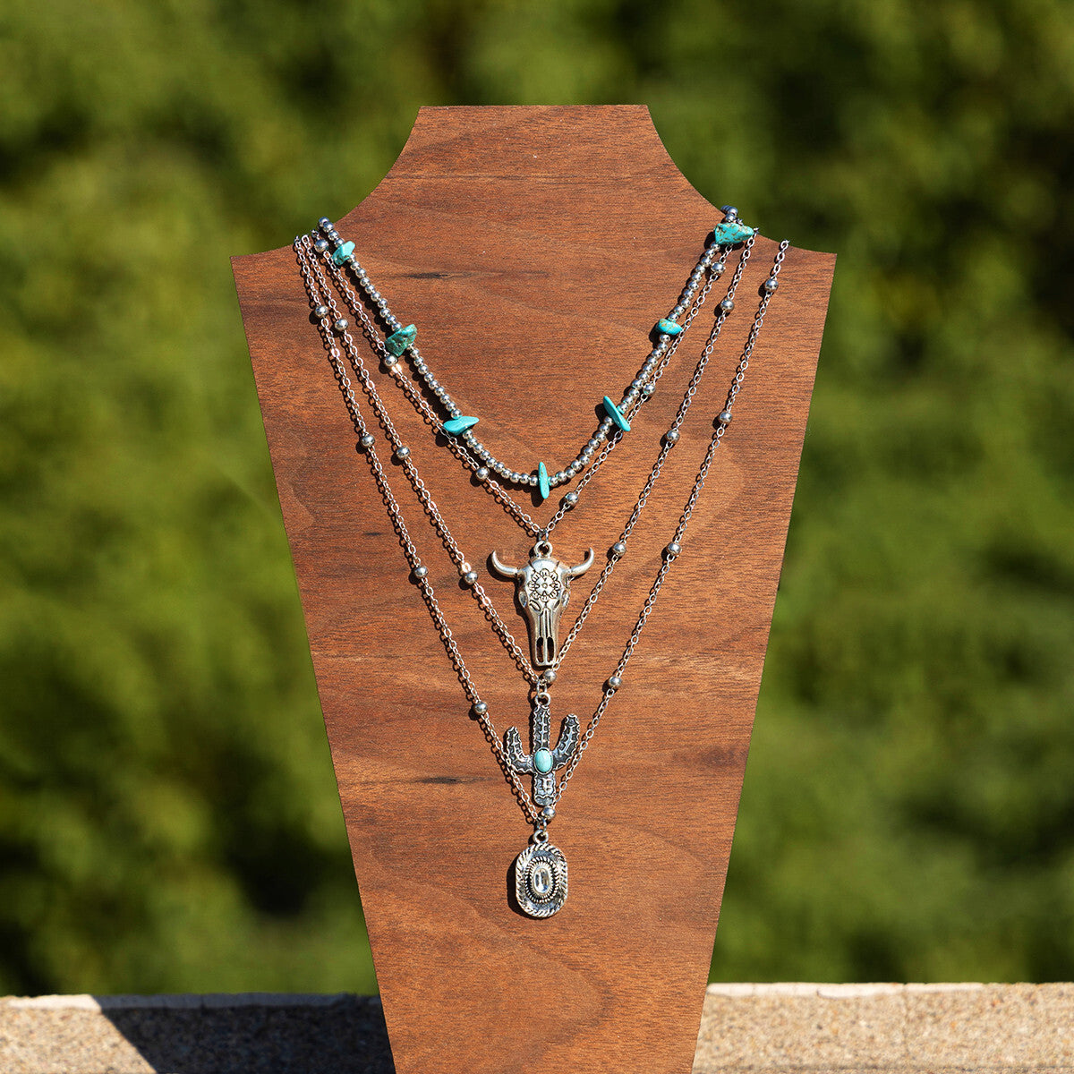 Necklace set with turquoise stones and metal pendants on a wooden stand with a blurred green background