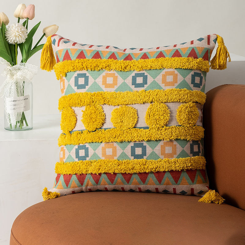 Decorative pillow with geometric pattern and tassels on a brown couch, with flowers in the background.