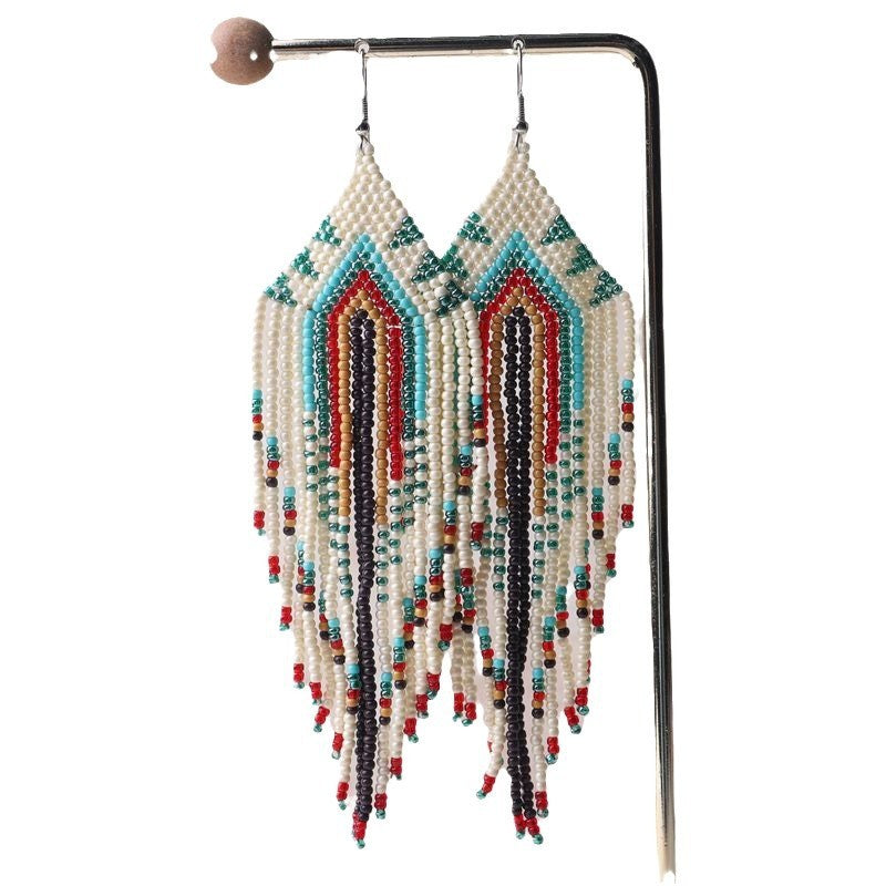 Beaded earrings with colorful fringe on a stand against a white background