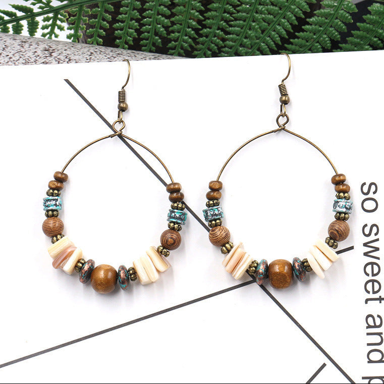 Pair of beaded hoop earrings on a white surface with green leaves in the background.