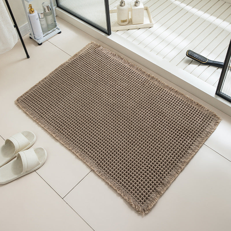 Beige doormat on a tiled floor with white slippers and a remote control nearby.