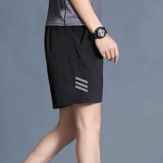 Person wearing black shorts with a brand logo and white sneakers on a gray background