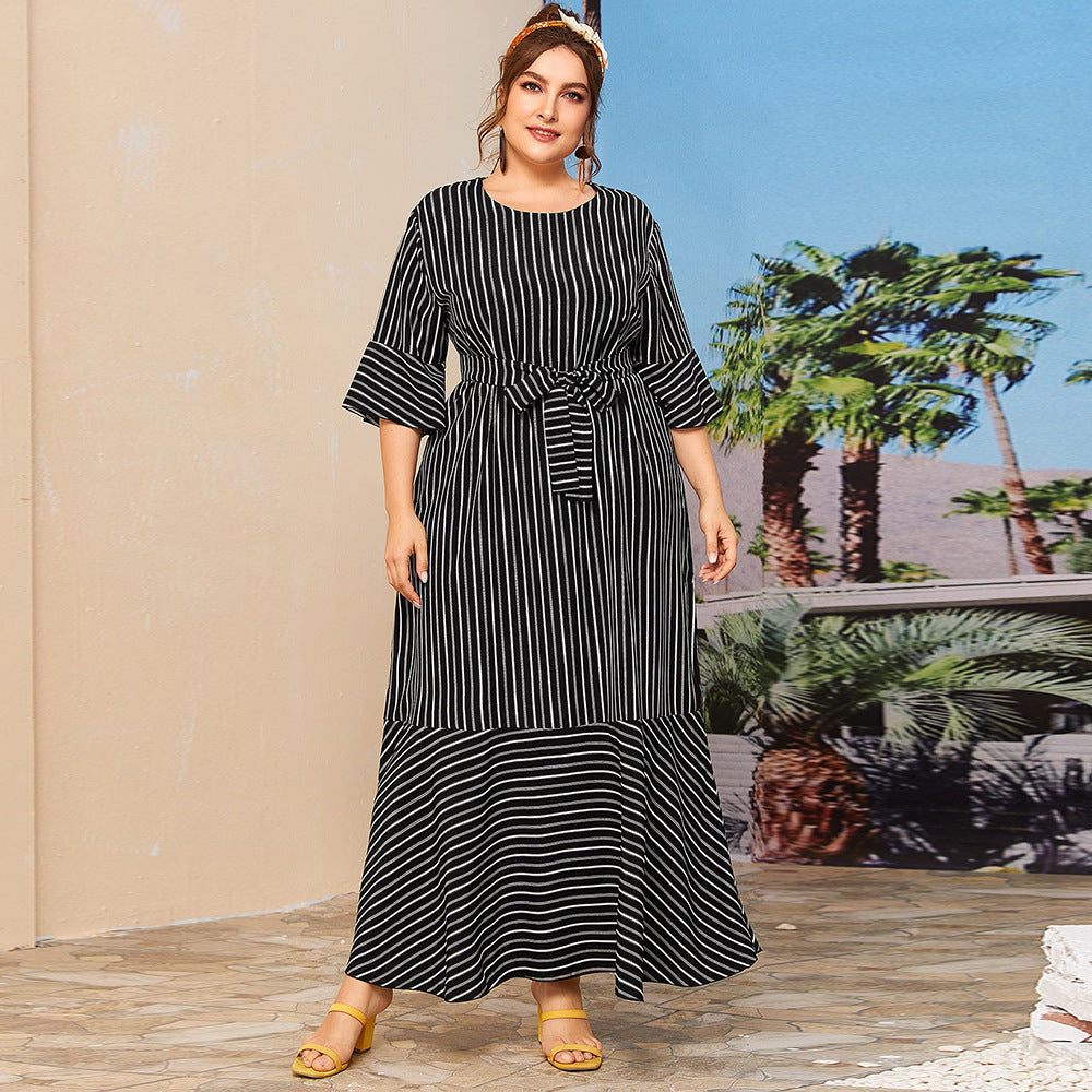 Woman wearing a black and white striped dress standing outdoors with palm trees in the background.