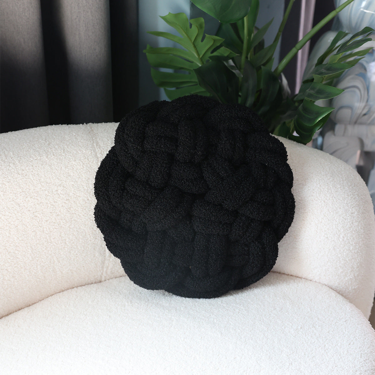 Black knitted pillow on a white couch with a plant in the background