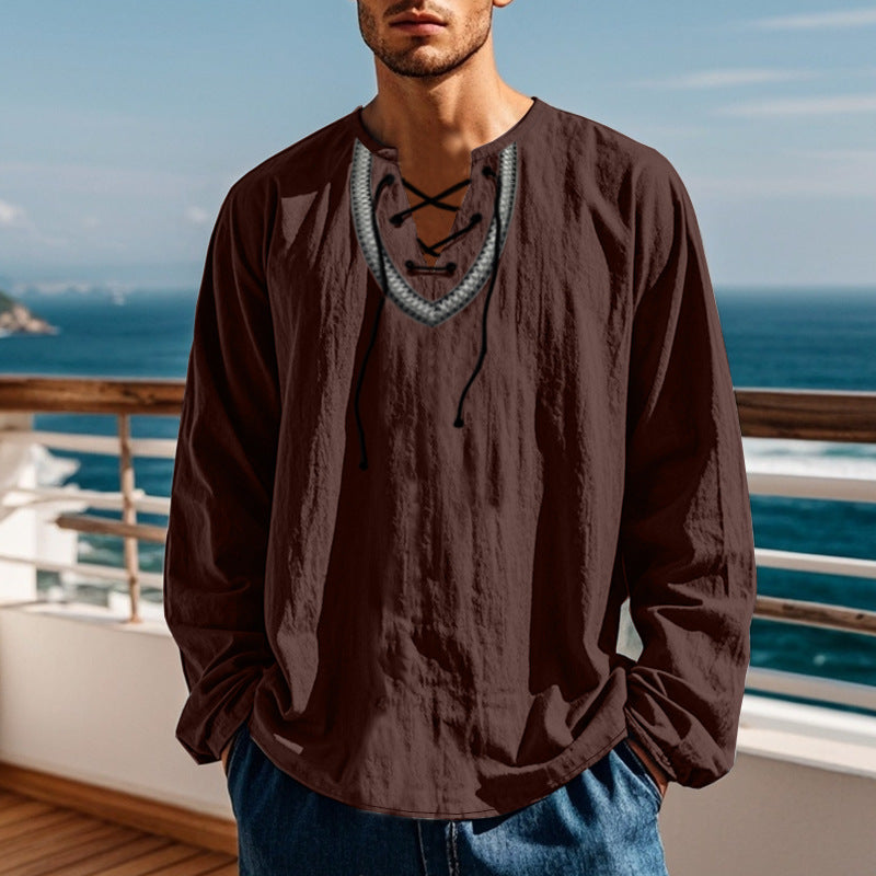 Man wearing a brown long-sleeve shirt with a decorative front panel, standing by a railing with ocean view.