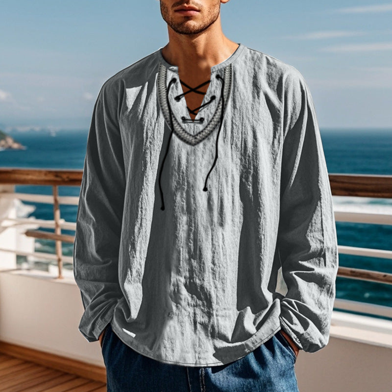 Man wearing a gray long-sleeve shirt with a decorative neckline by the ocean.