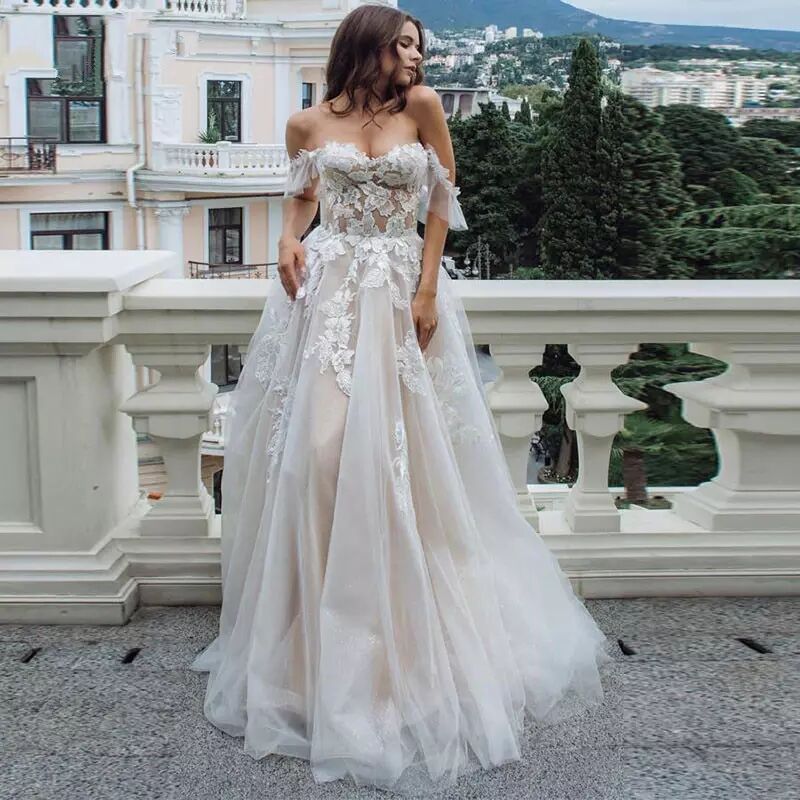 Woman in a white lace wedding dress standing on a balcony with a scenic background