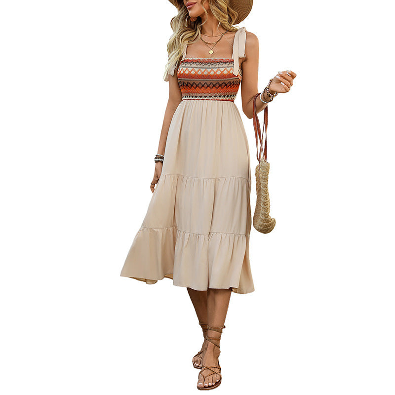 Woman wearing a beige dress with a patterned top, holding a straw bag on a white background