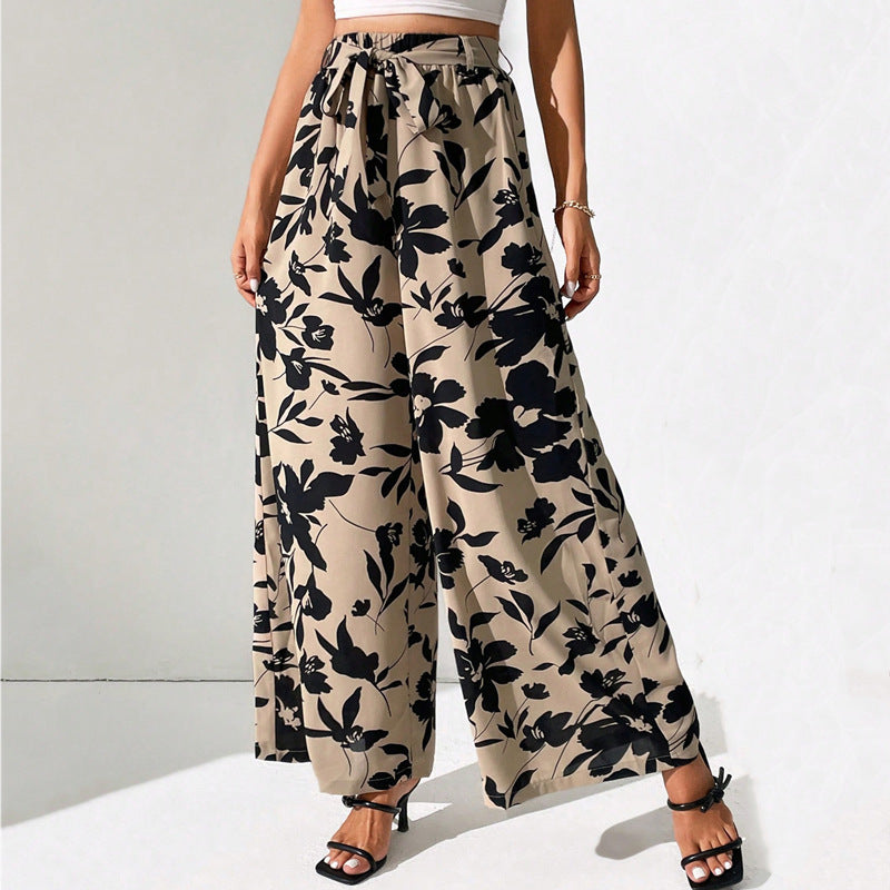 Beige wide-leg pants with black floral pattern worn by a person on a white background