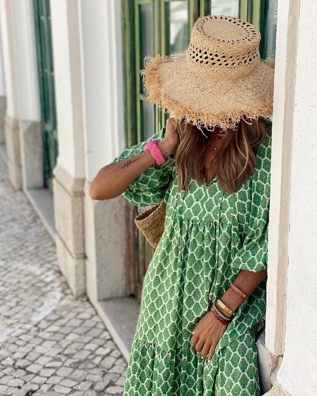 Person wearing a green patterned dress and straw hat in an urban setting