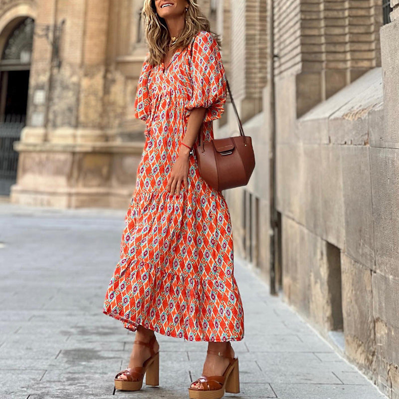 Woman in an orange patterned dress with a brown handbag walking on a street.