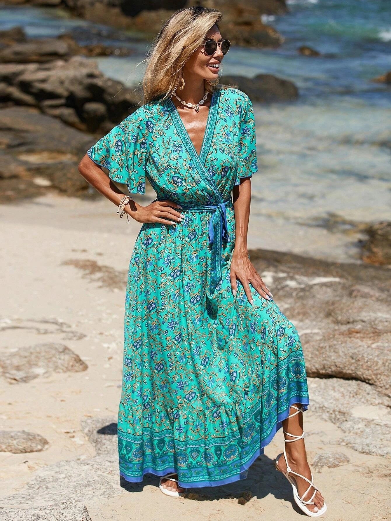 Woman in a green patterned dress standing on a rocky beach.