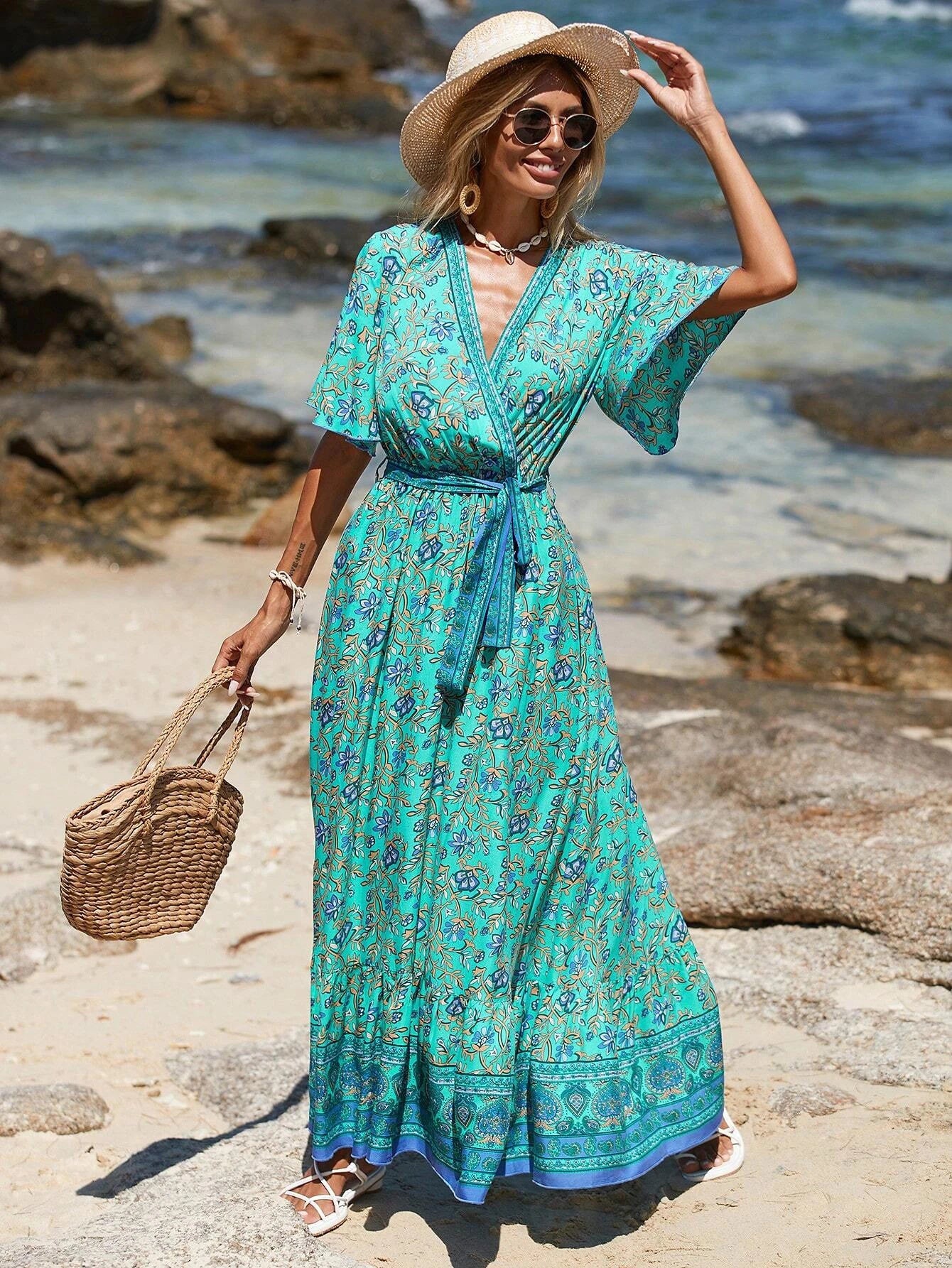 Woman in a teal dress with floral pattern standing on a beach.