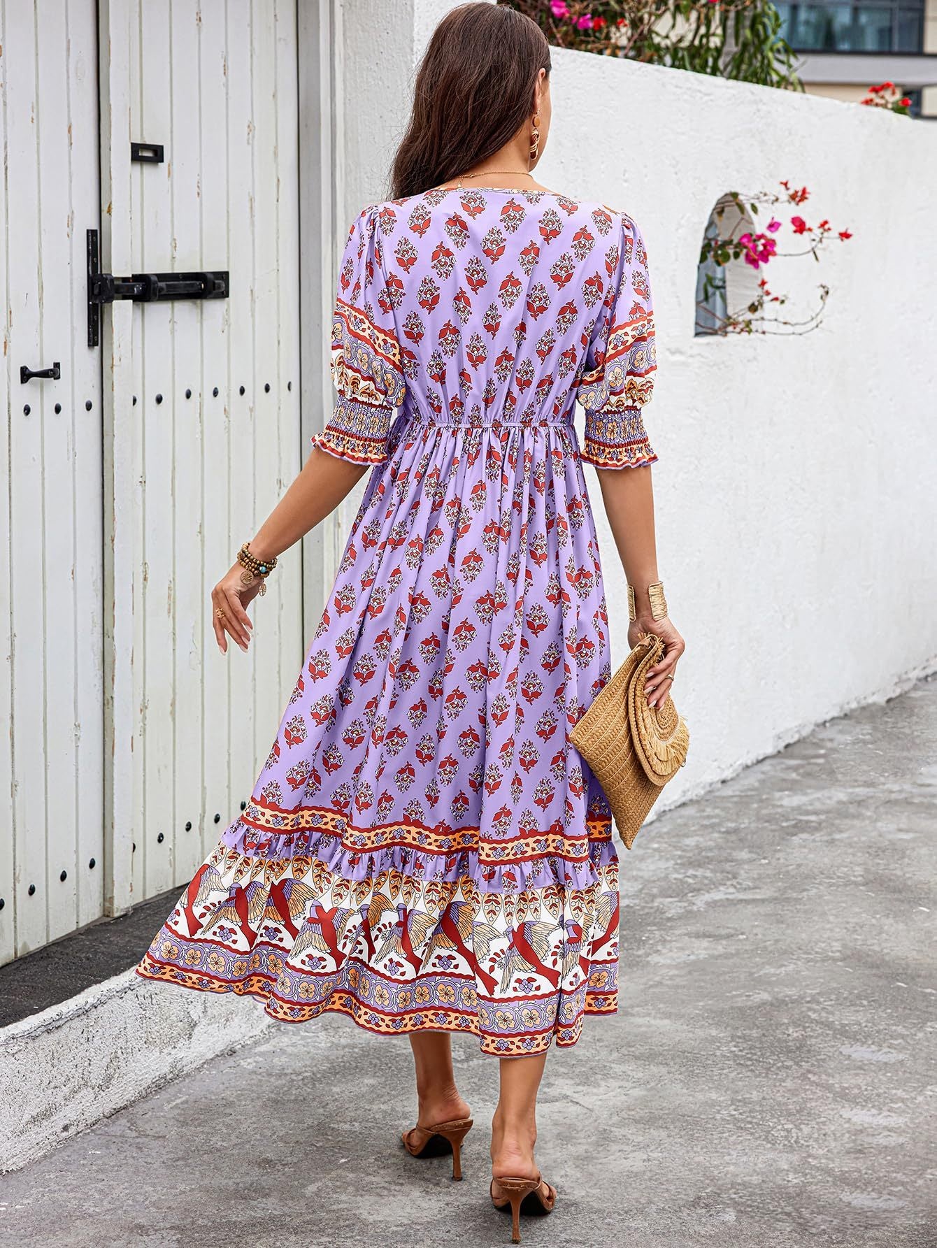 Woman wearing a purple floral dress walking outdoors near a white wall.