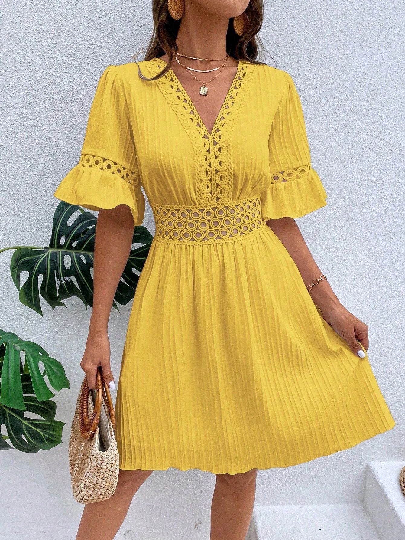 Woman wearing a yellow dress with lace details against a white wall.