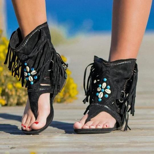 Black fringe sandals with shell embellishments on a beach setting