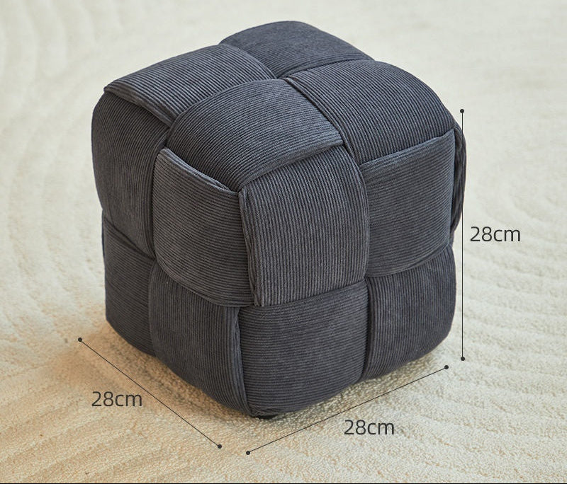Dark grey cube-shaped ottoman with measurements on a beige carpet