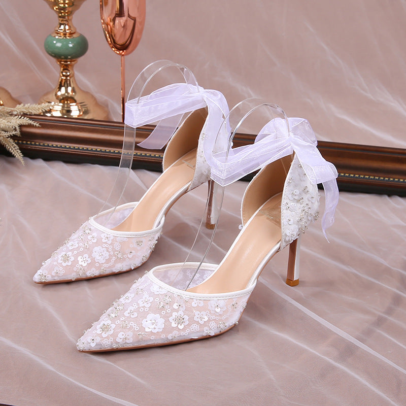 White lace high-heeled shoes with sheer ribbon on a reflective surface.