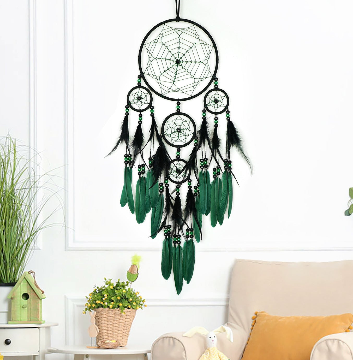 Dreamcatcher with green feathers hanging above a living room with a couch and plants.