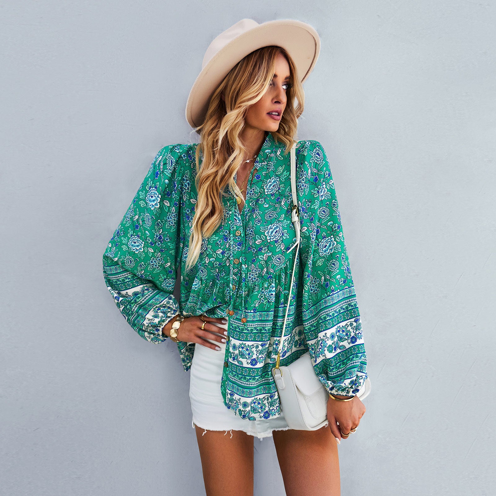 Woman wearing a green patterned blouse and white shorts against a gray background