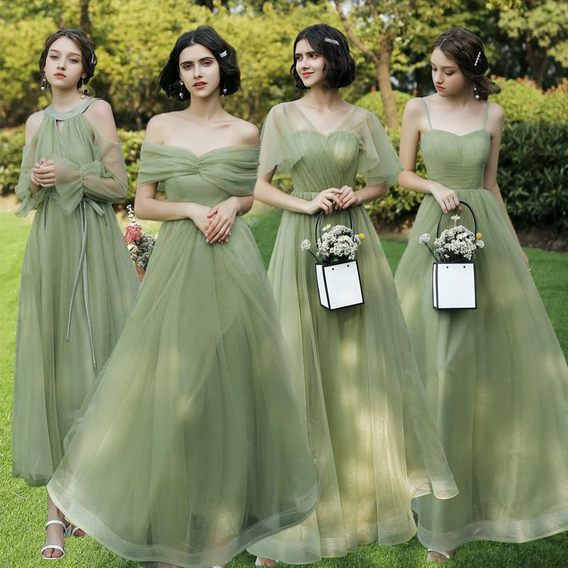 Four women in matching green dresses standing outdoors on grass.