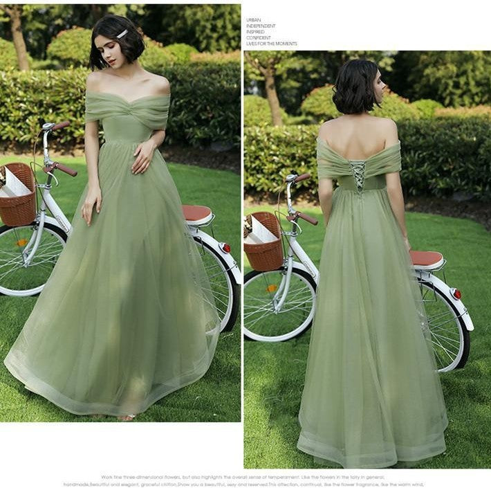 Woman in a green off-shoulder dress standing next to a bicycle on grass.