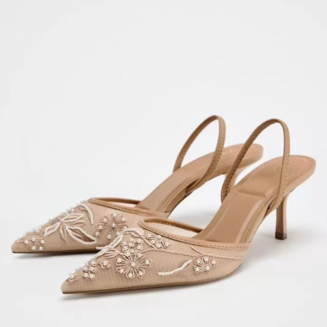 Beige high-heeled shoes with floral embroidery on a white background