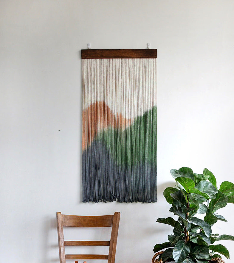 Woven wall art with a mountain design in a room with a plant and chair.