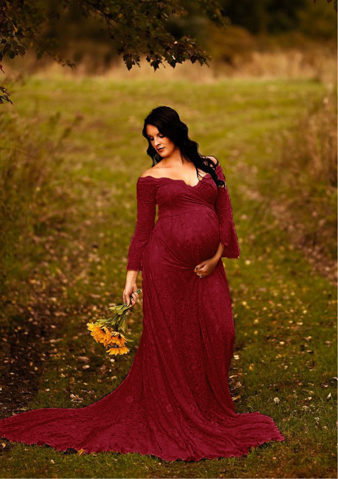 Pregnant woman in a red dress standing in a natural setting with trees and grass.