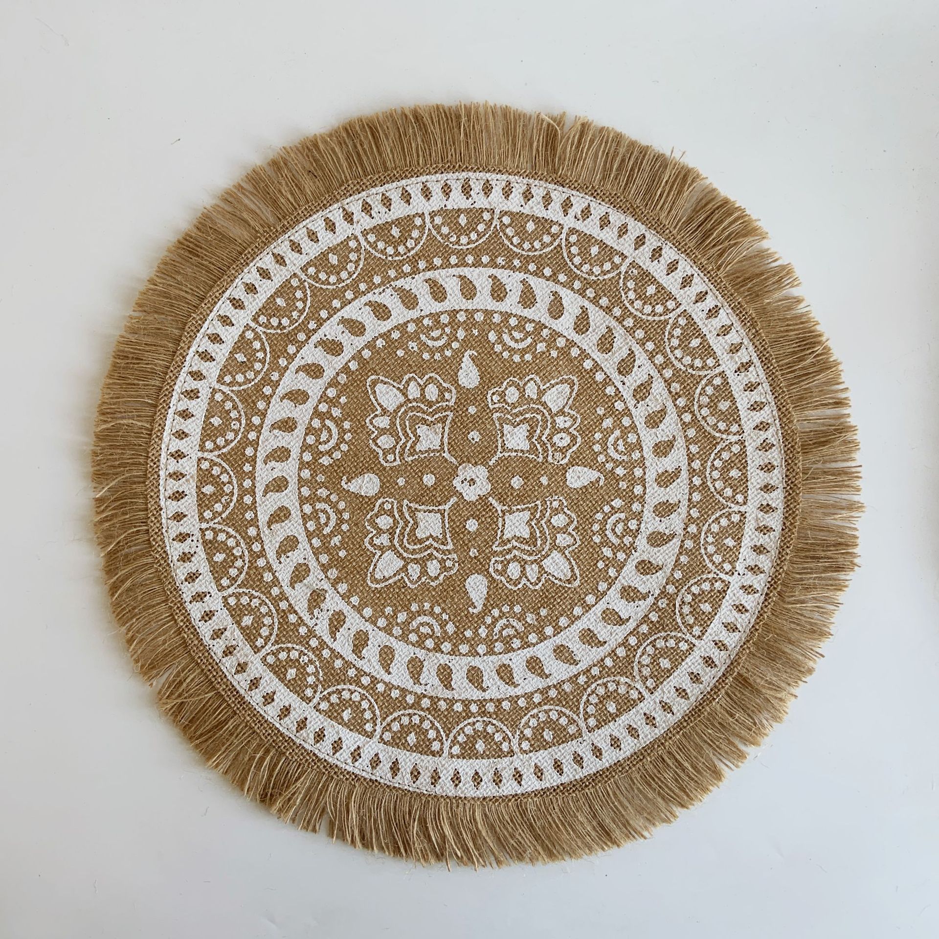 Round placemat with white pattern and brown fringes on a white background