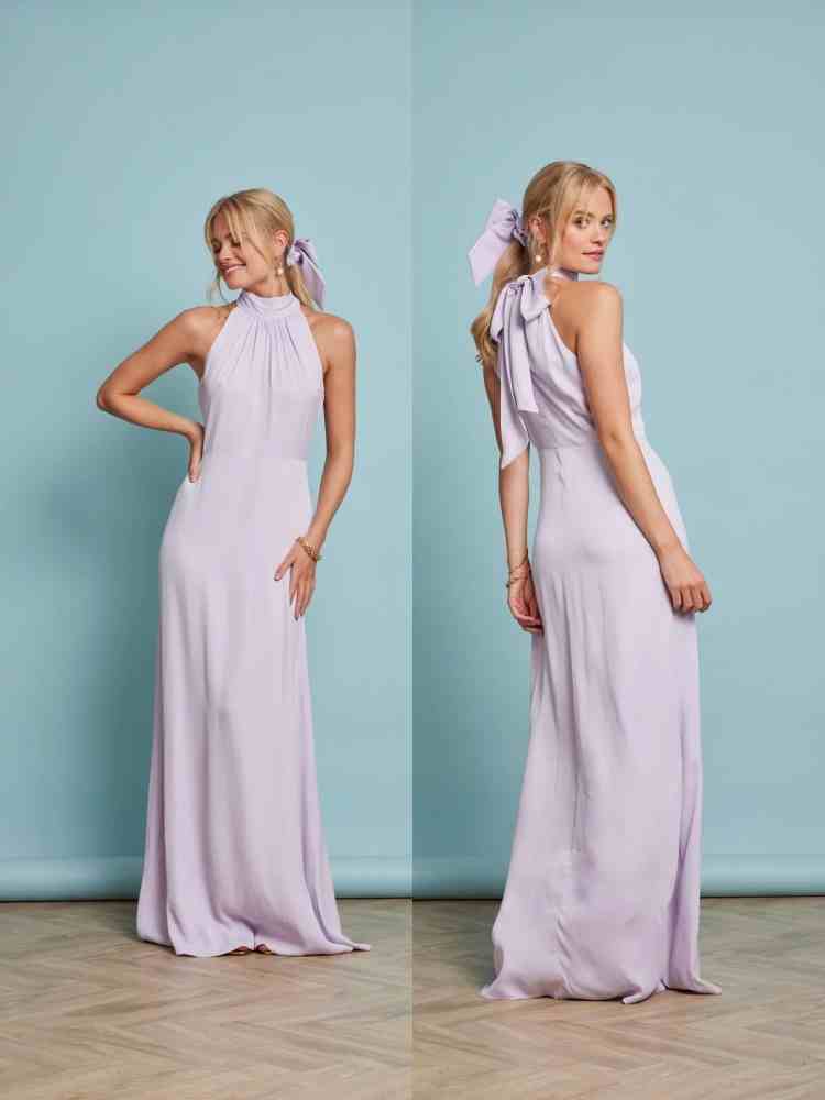 Woman wearing a light purple halter neck dress with a bow detail, standing against a light blue wall.