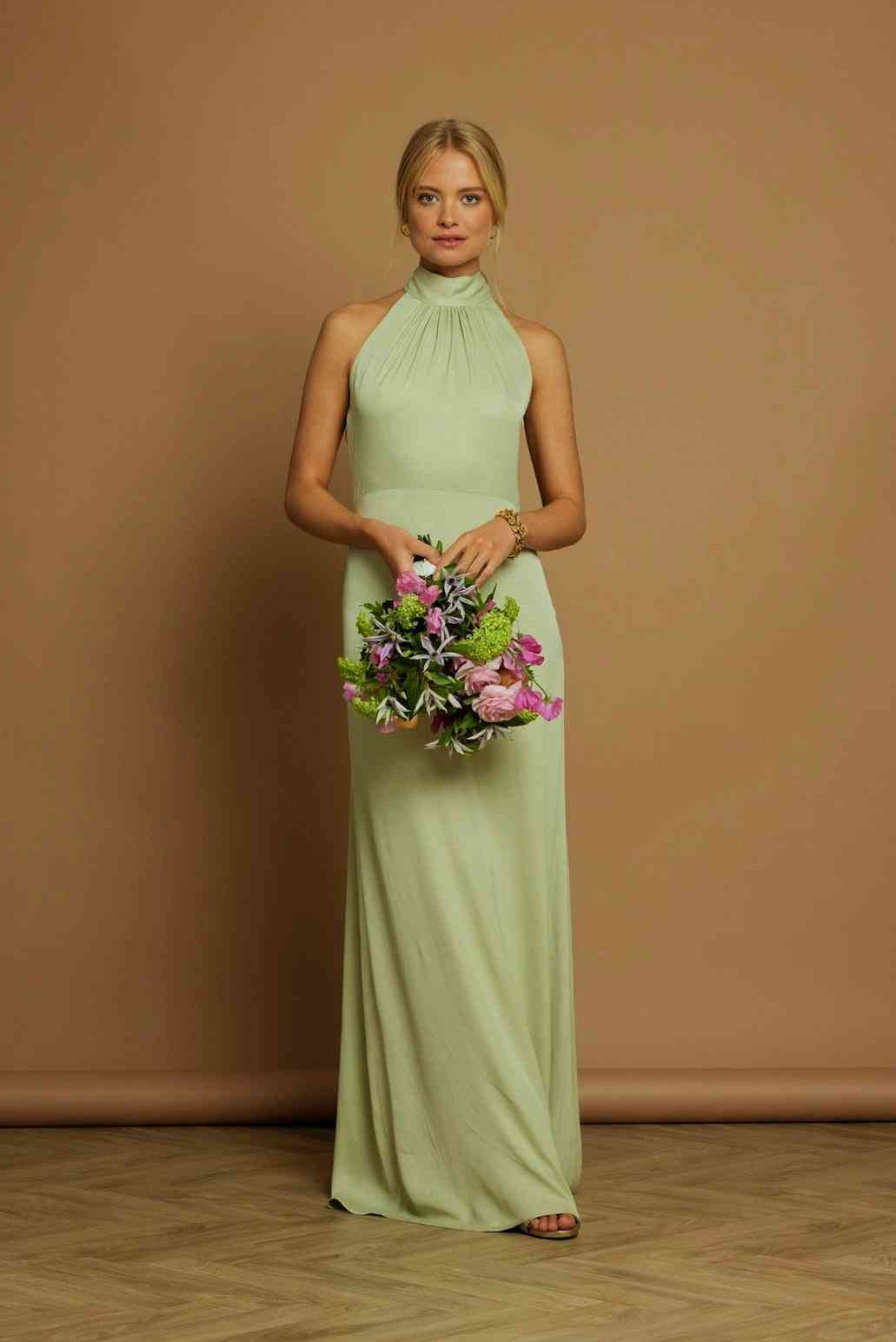 Woman in a long light green dress holding flowers against a brown background