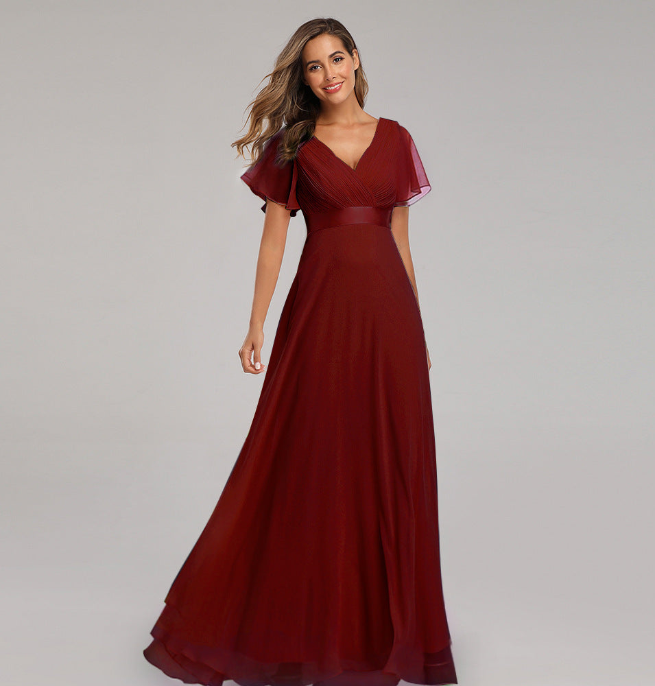 Woman wearing a burgundy evening gown with ruffled sleeves on a gray background