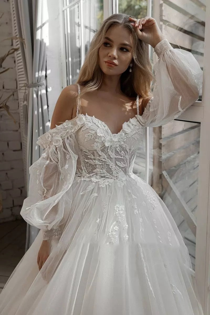 Woman wearing a white wedding dress with long sleeves in a softly lit room.