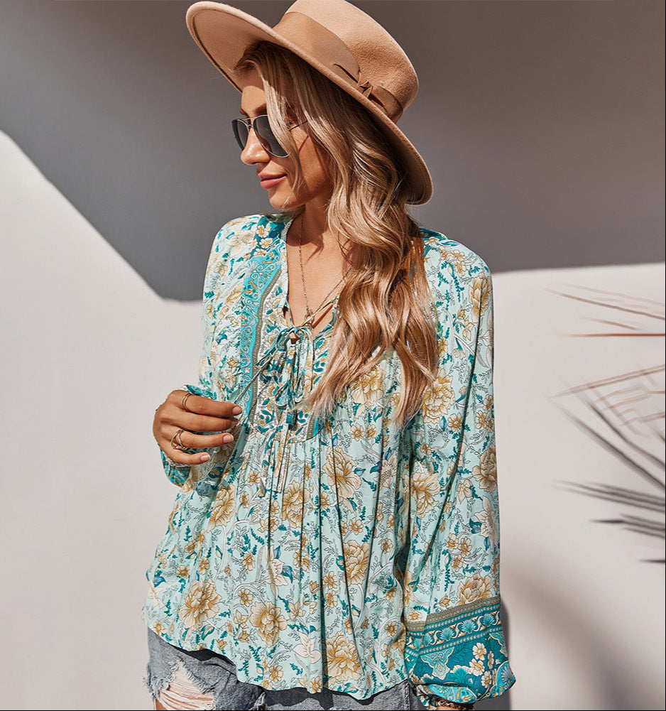 Woman wearing a floral blouse and beige hat with sunglasses, standing against a neutral background.