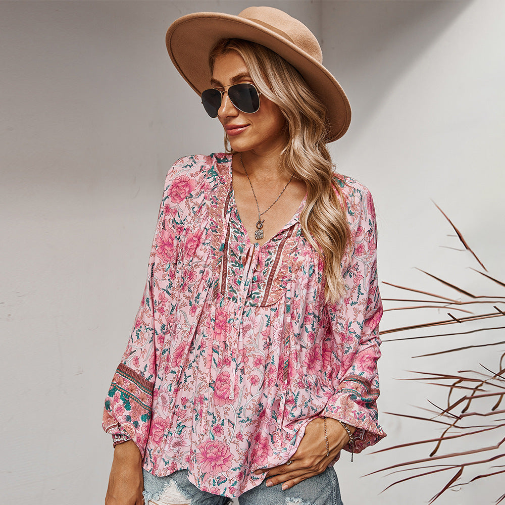 Woman wearing a pink floral blouse, beige hat, and sunglasses against a neutral background