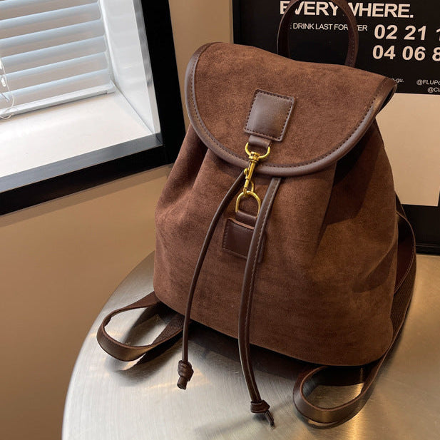 Brown suede backpack on a metallic surface with a poster in the background.