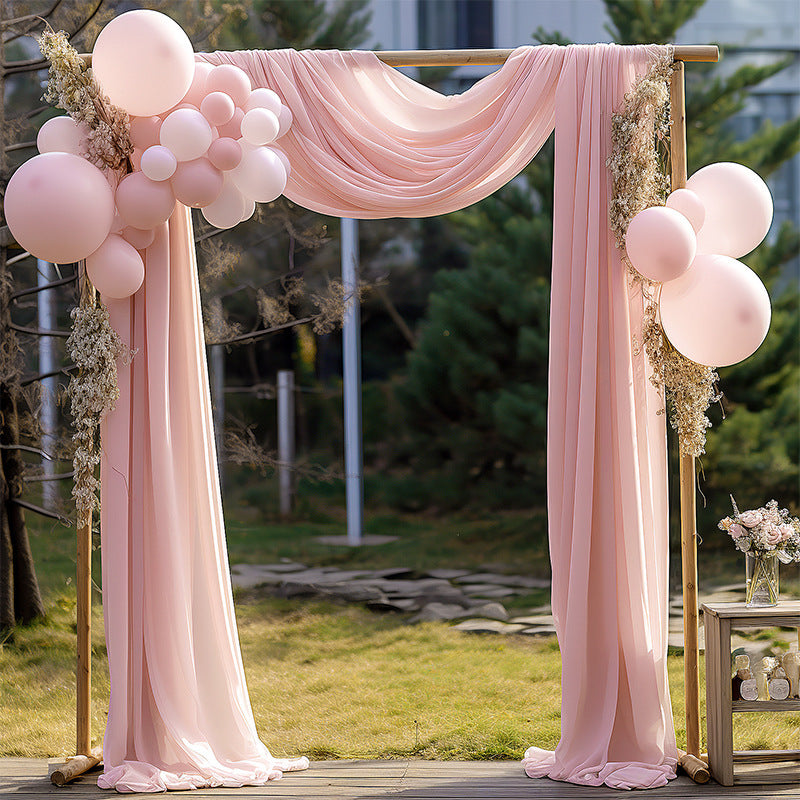 Decorative arch with pink curtains and balloons in an outdoor setting