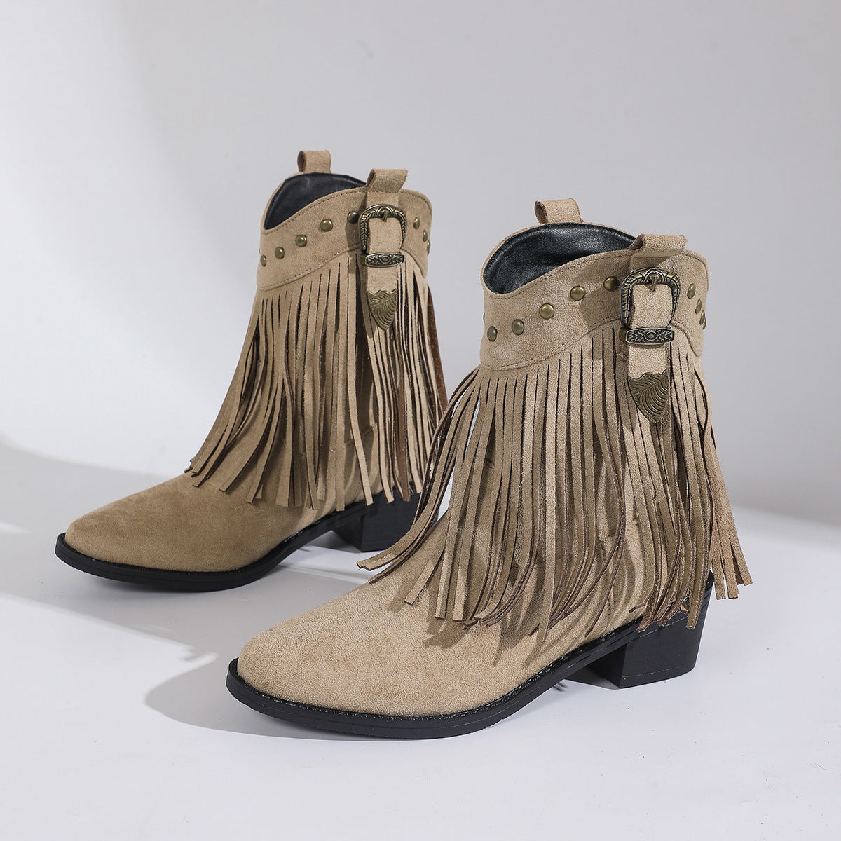 Pair of beige fringe boots with black soles on a light gray background