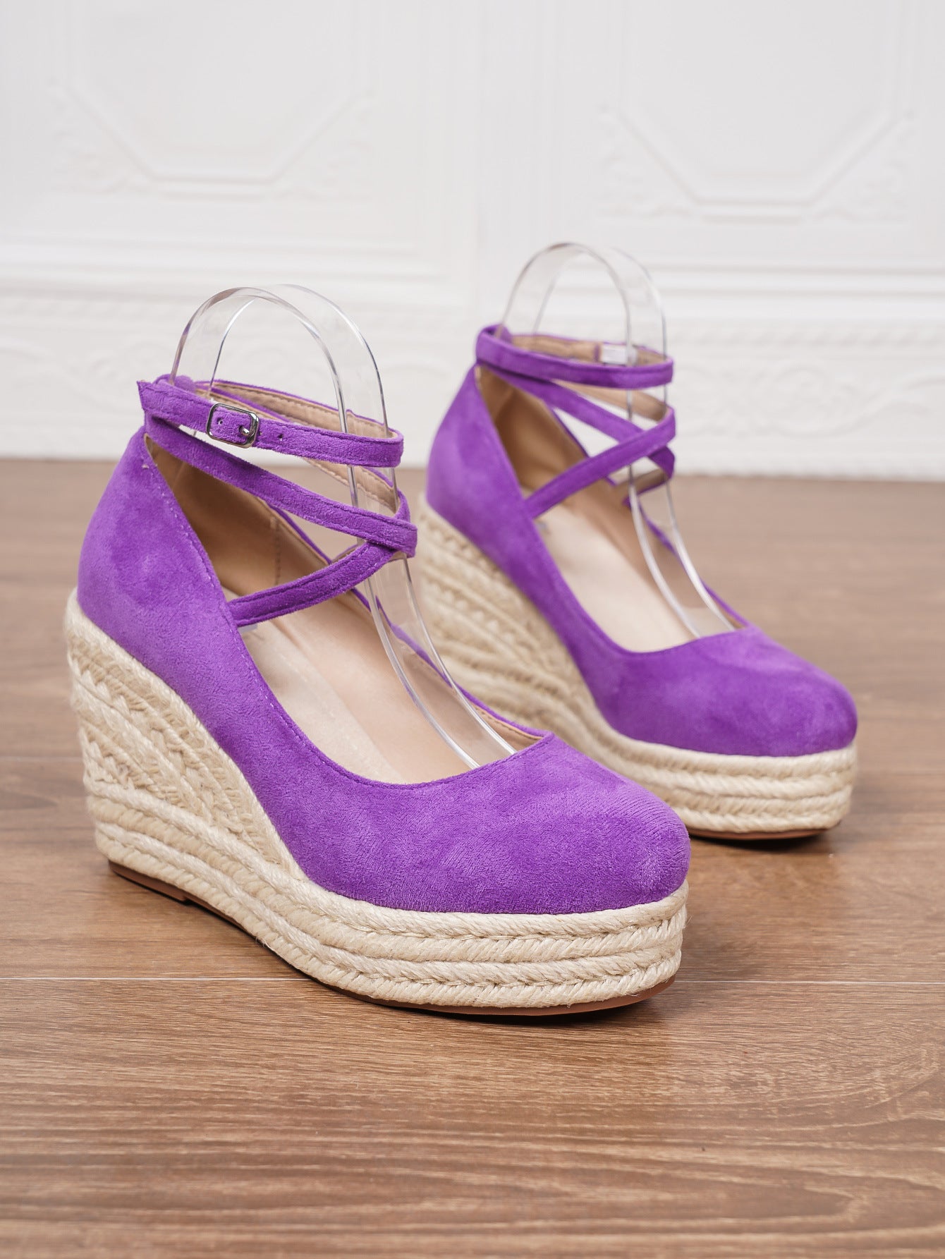 Purple wedge sandals on a wooden surface with a white background