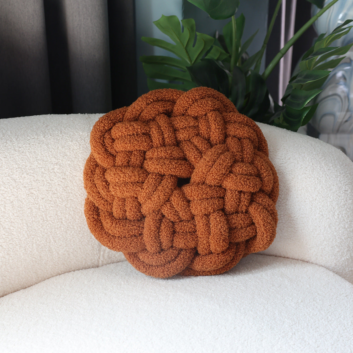 Brown braided knot pillow on a white couch with plants in the background