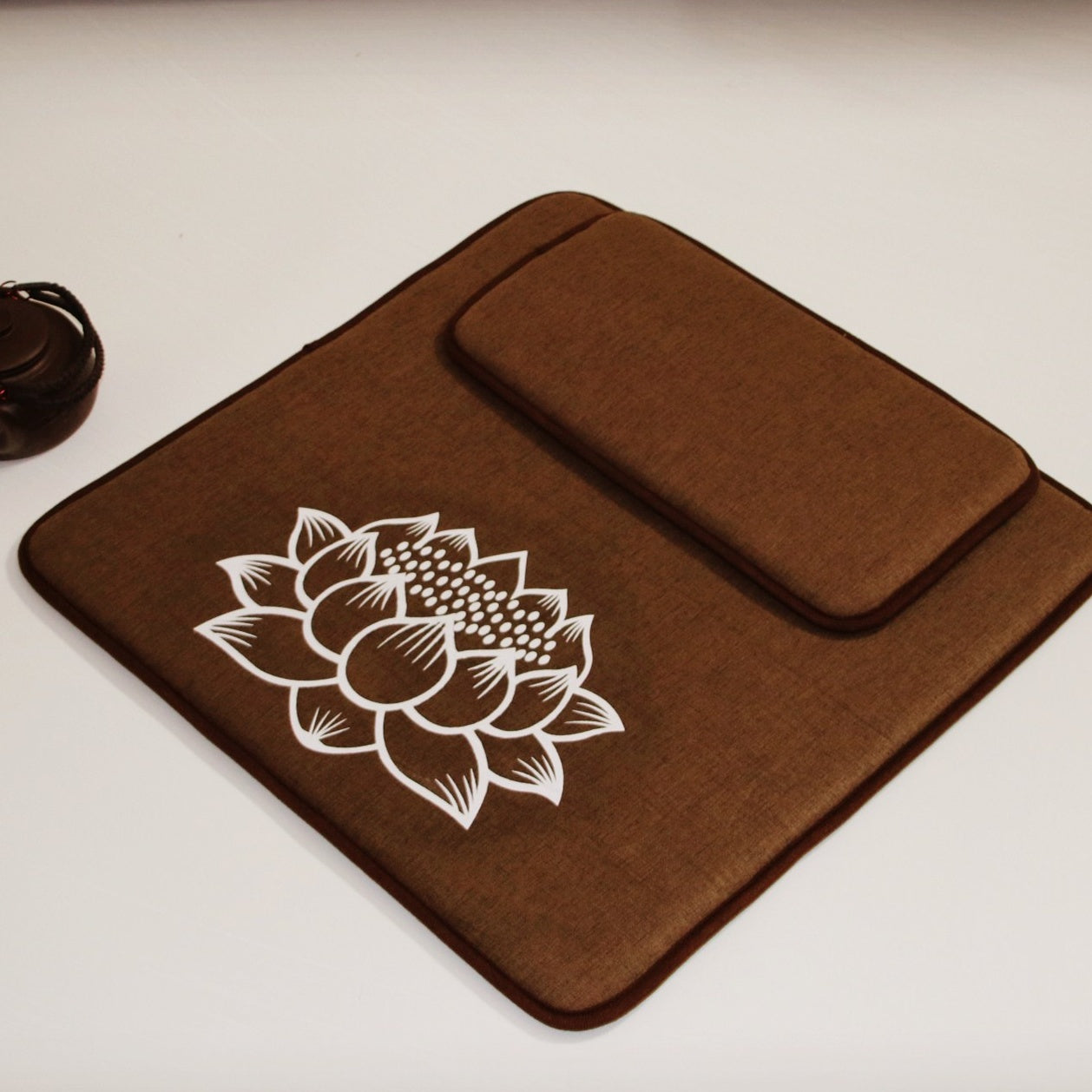 Brown fabric mat with a white lotus flower design on a light background