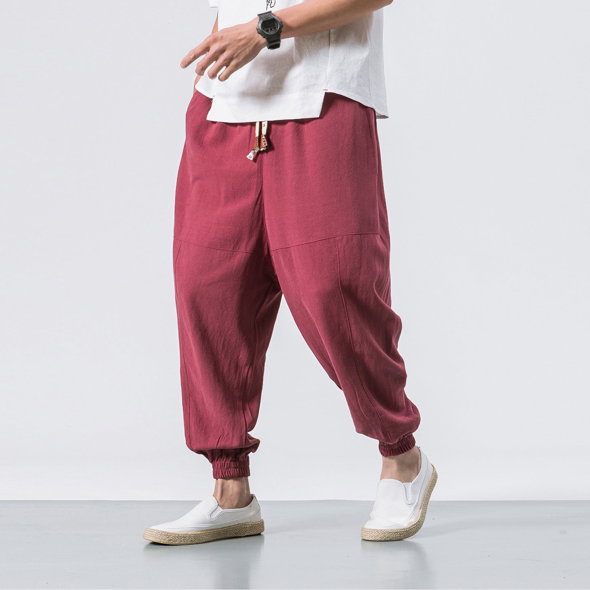 Person wearing maroon jogger pants and white sneakers on a plain background