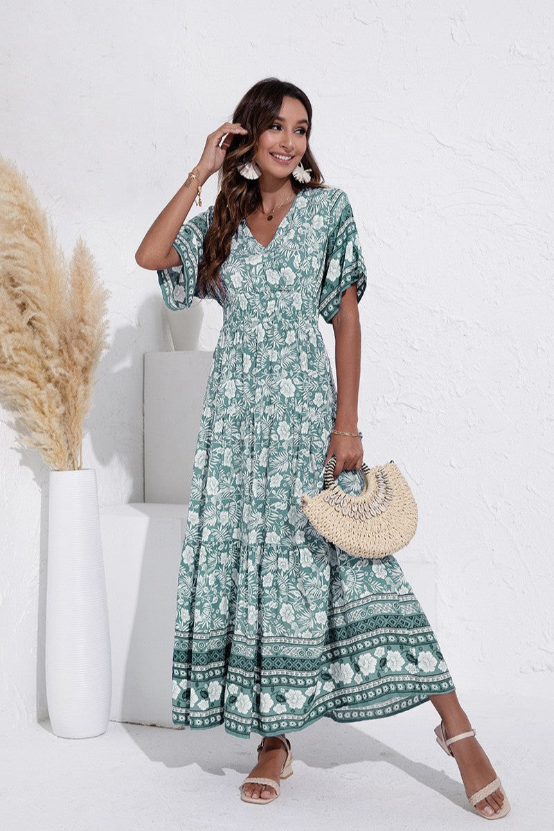 Woman wearing a green floral dress holding a straw bag against a white background