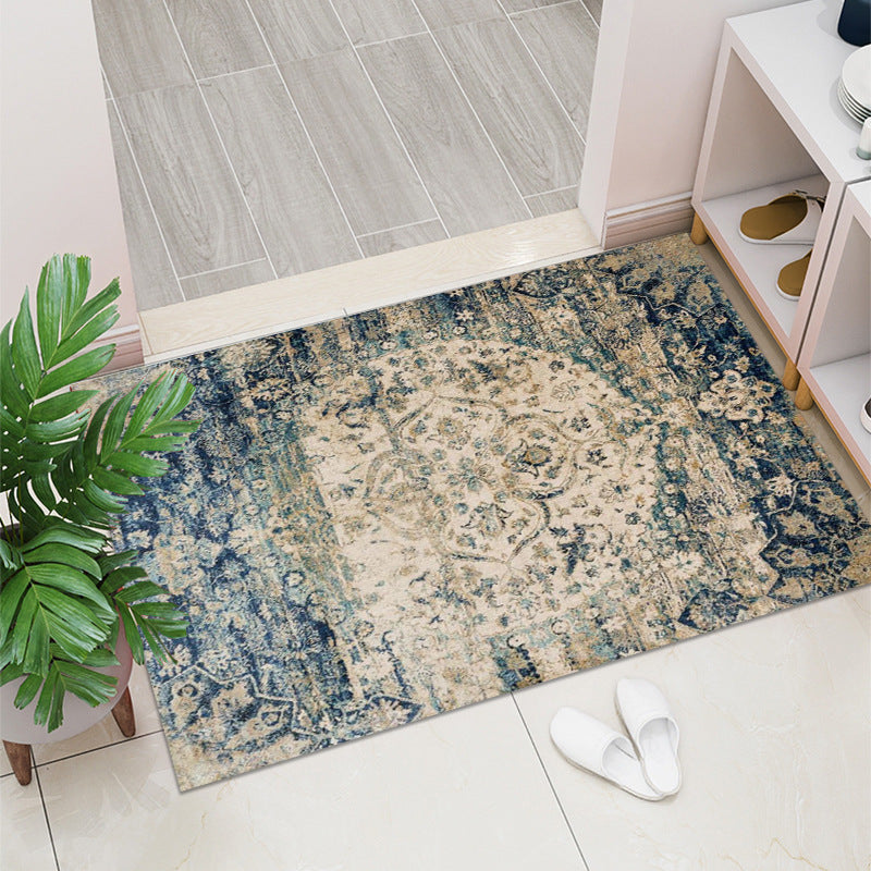 Decorative rug with a floral pattern on a tiled floor next to a plant and white slippers.