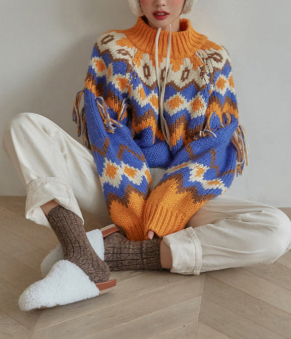 Person wearing a colorful patterned sweater sitting on a wooden floor.