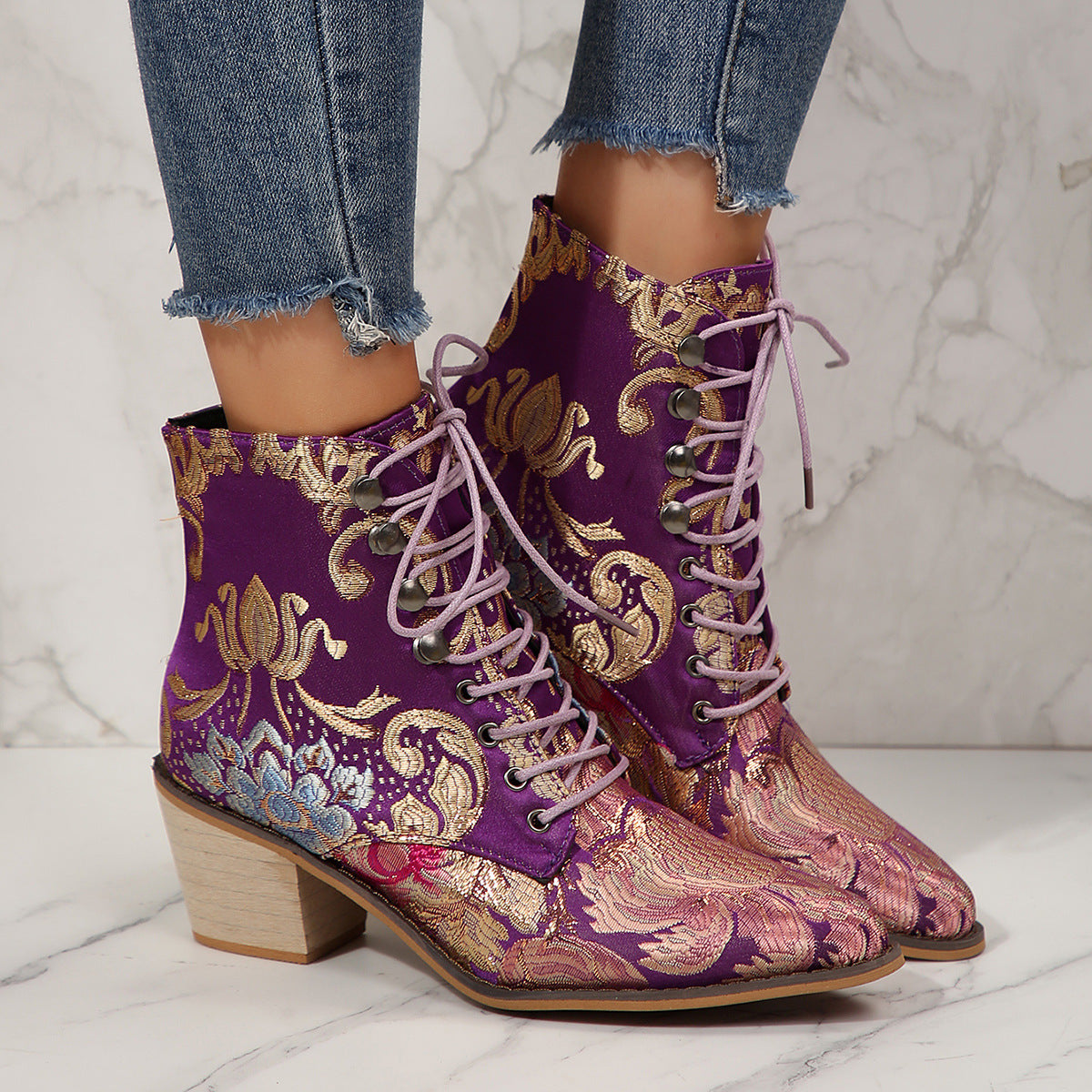 Purple embroidered boots with gold patterns worn with jeans on a marble floor.