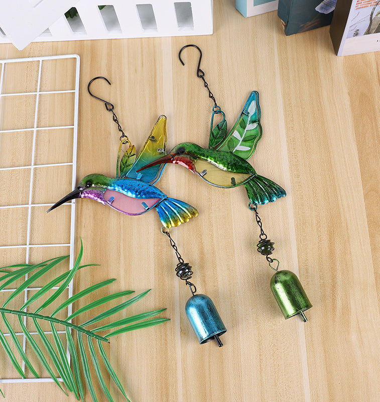 Colorful hummingbird-shaped hanging ornament with bells on a wooden surface.