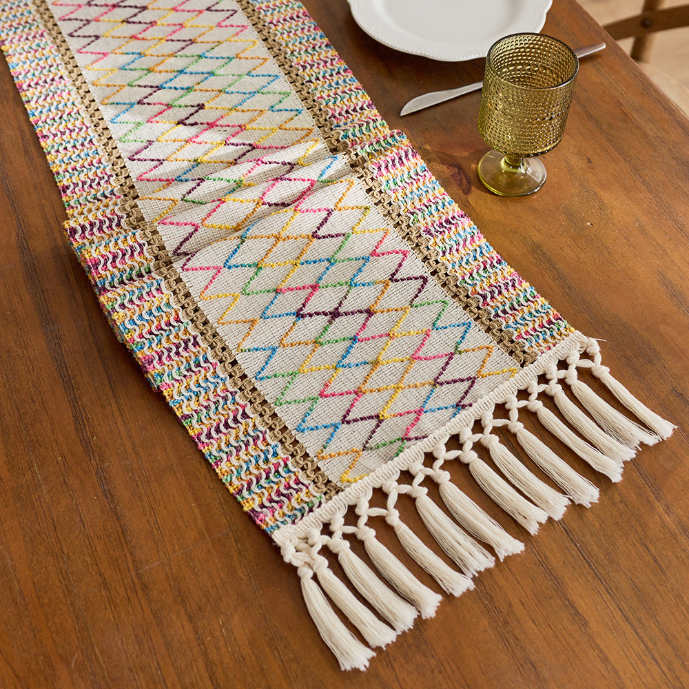 Colorful woven table runner with tassels on a wooden table.